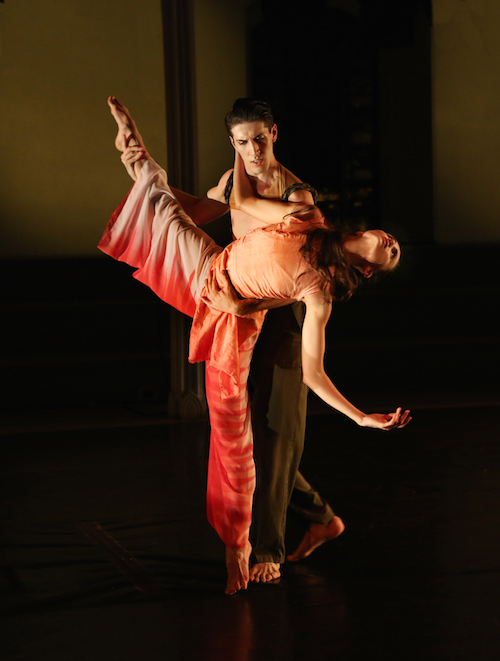 A male dancer holds his female partner's leg as leans back in a suspended back bend